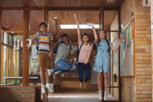 Excited classmates jumping with grade cards in corridor